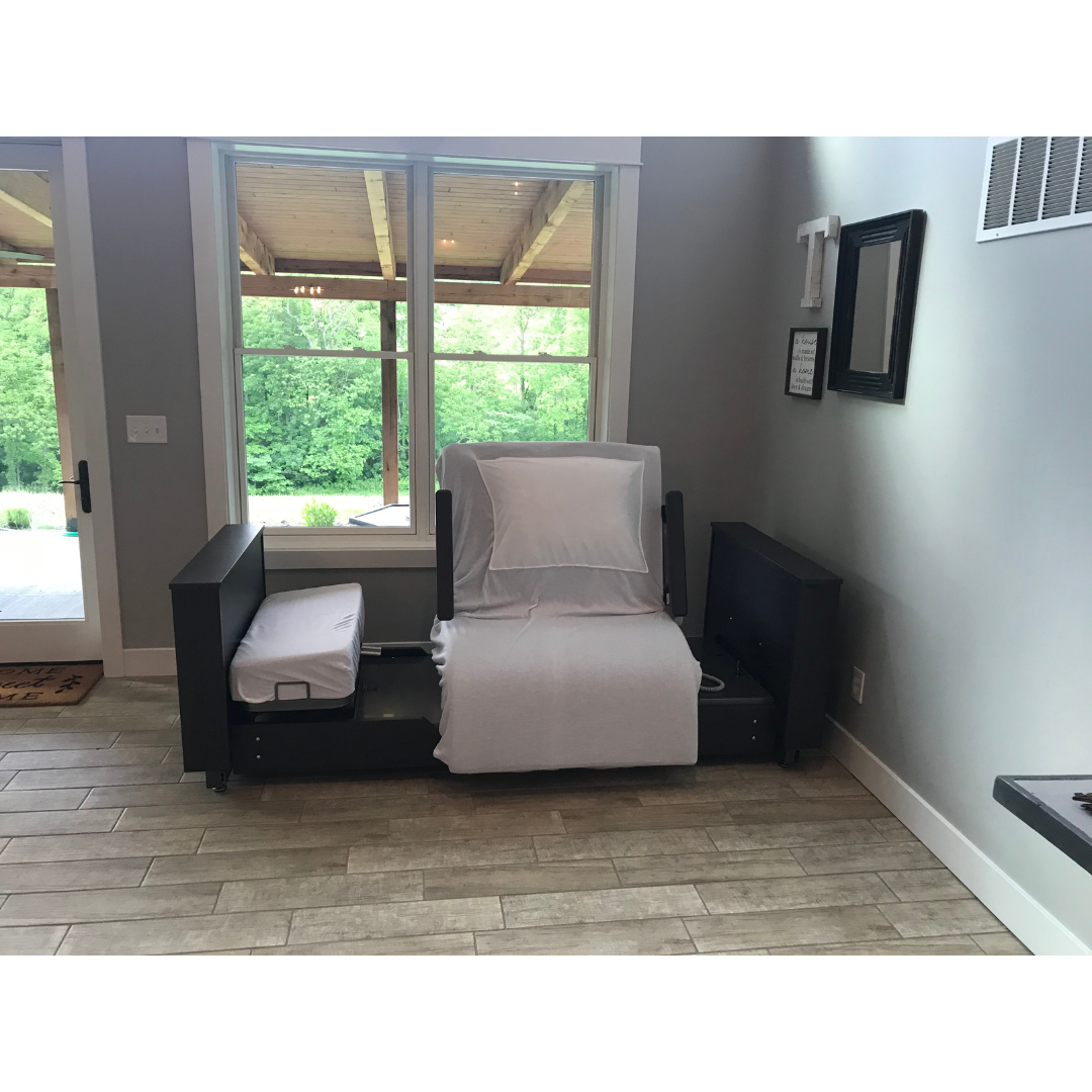 A Med-Mizer ActiveCare Rotating Hospital Bed with light bedding sits in a modern room near a large window overlooking a wooden patio and lush greenery, complemented by light wood floors and neutral-colored walls.