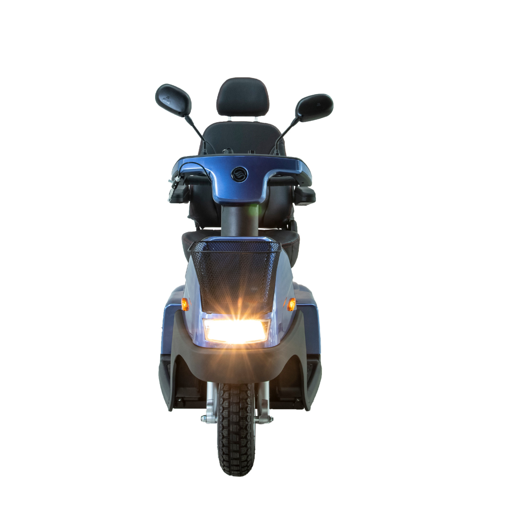 A front view of the Afikim Afiscooter C3 HD, a blue mid-size 3-wheel mobility scooter, with handlebars featuring mirrors and a cushioned seat. It has the headlight on, includes a mesh basket, and is isolated on a white background.