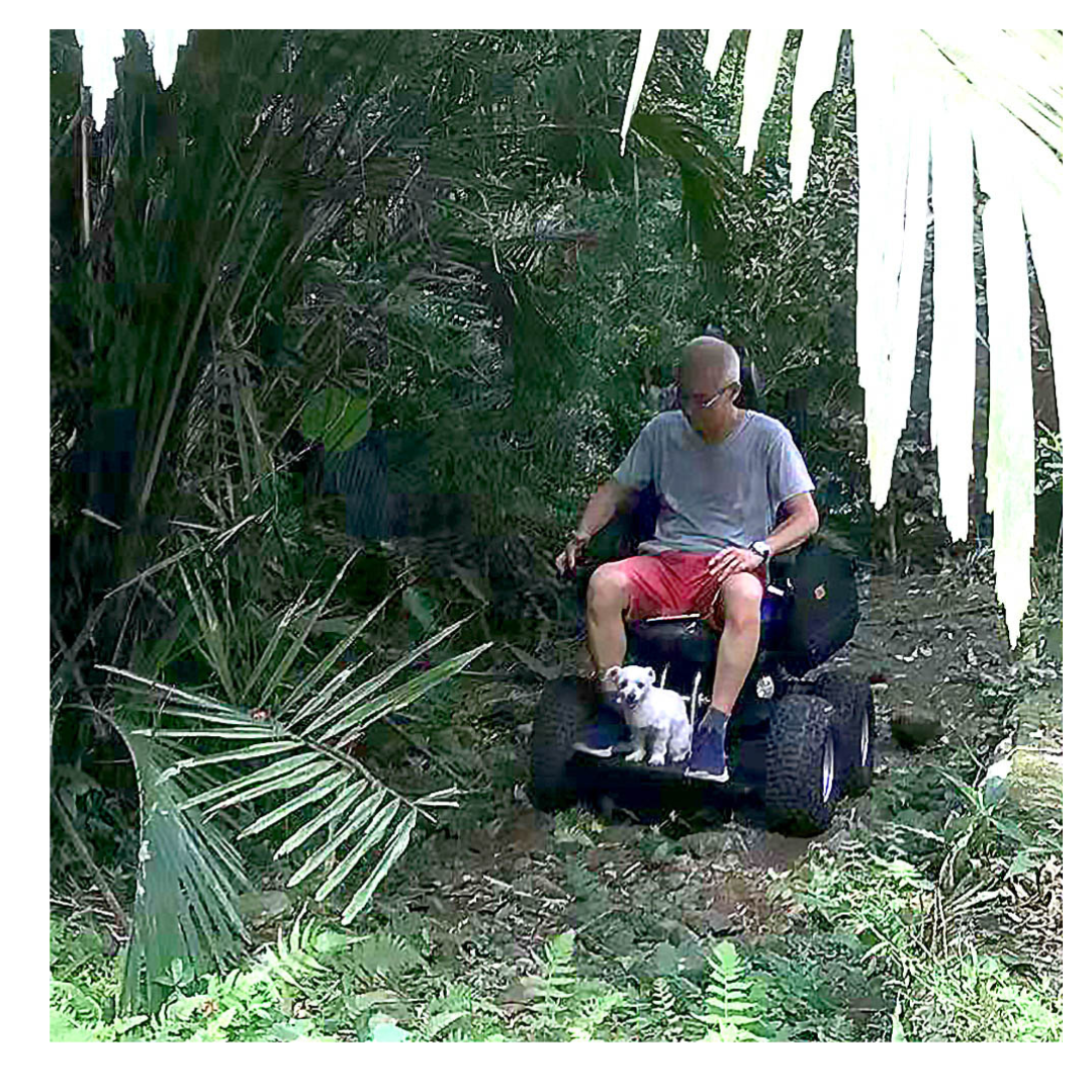 A man in a gray shirt and red shorts rides a Wheelchair88 All-Terrain Stair Climbing 4x4 Recreational Electric Vehicle with his small white dog on his lap, navigating through dense, leafy greenery.