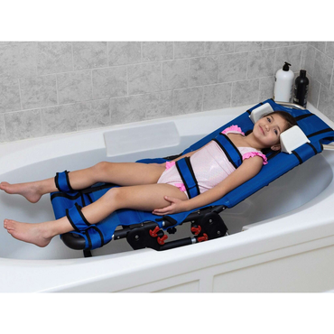 A smiling girl in a swimsuit lies on the Circle Specialty Pediatric Anchor Bath Chair with safety straps, relaxing in a white tub. The adjustable chair offers support and comfort. Shampoo and soap bottles rest on the tub’s edge.
