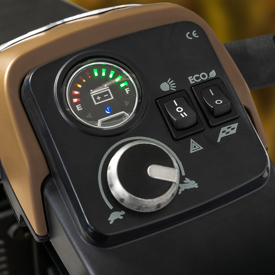 Close-up of the Pride Baja® Bandit 4 Wheel Scooters dashboard, showcasing a fuel gauge, toggle switches, and a large control dial. Designed for off-road excursions, it features symbols like a rabbit and turtle for varied terrain settings.