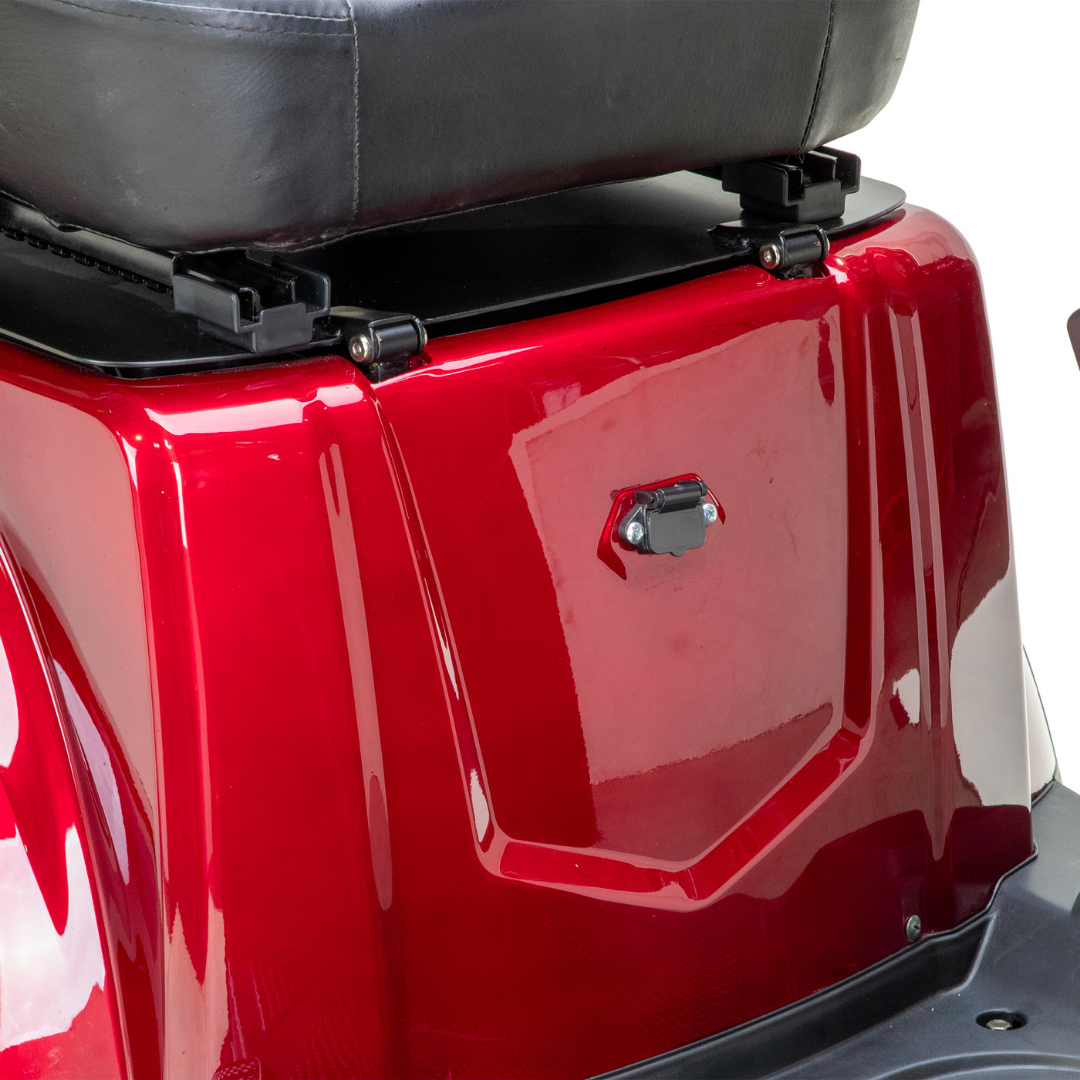 Close-up of the rear section of a red Bespoke Legacy Recreational 3-Wheel Scooter, showing its shiny metal surface, black latch, underside of the cushioned seat, and part of the electric lighting system.
