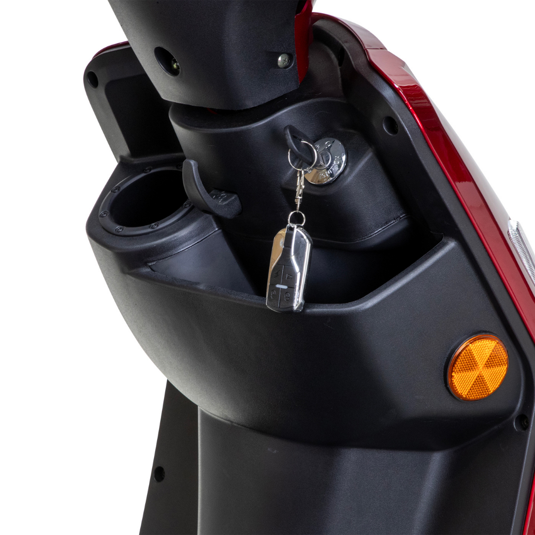 Close-up of a Bespoke Legacy Recreational 3-Wheel Scooter’s ignition area with a key inserted, black cup holder on the left, and storage compartment. Its 600-watt motor powers a red and black frame with an orange reflector on the side.