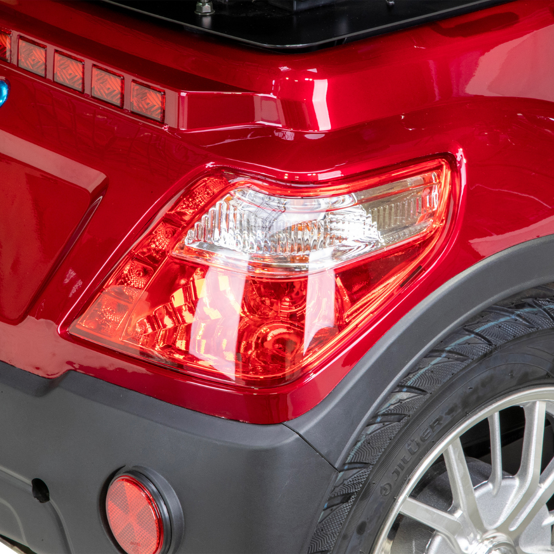 Close-up of the rear right tail light and wheel of a shiny red Bespoke Legacy Recreational 3-Wheel Scooter, showcasing the reflective tail light, textured tire, and hinting at its powerful 600-watt motor.