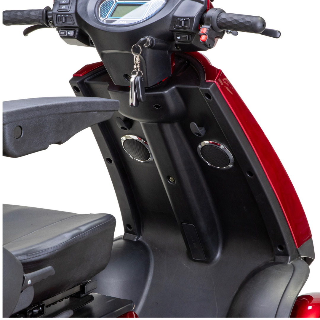 Close-up of the control panel, handles, and seat of the Bespoke Platinum Recreational 4-Wheel Scooter with Electric Brake Assist; keys hang from the ignition and two round speakers are visible below the dashboard.
