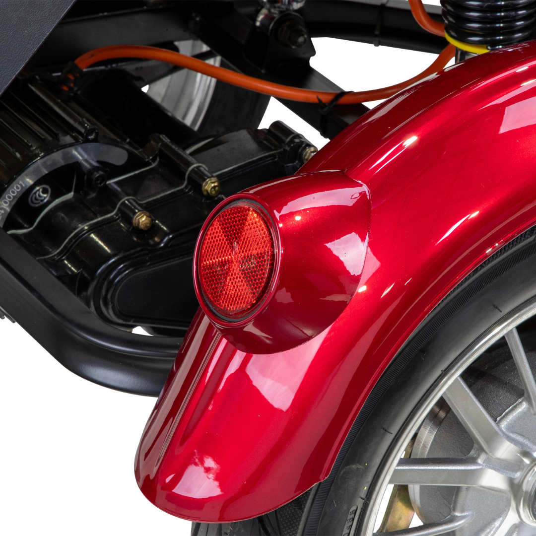 Close-up of the Bespoke Regal Recreational 3-Wheel Scooters shiny red fender with a round red reflector, visible tire and metal wheel, orange wires, engine components in the background, and a powerful 600-watt motor.