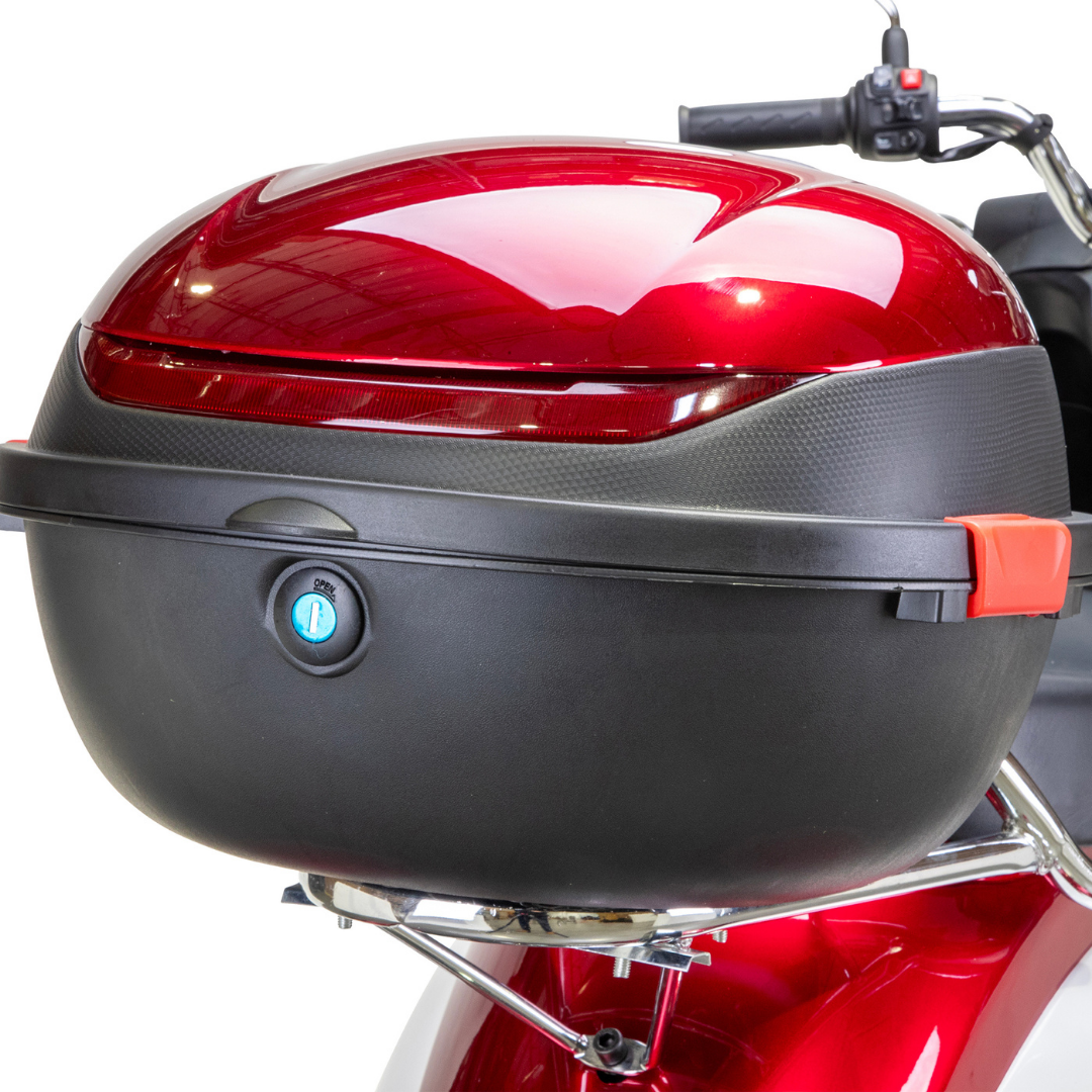 A close-up of the shiny red Bespoke Supreme Euro-Style Recreational 3-Wheel Scooter with Electric Brake Assist, featuring a black and red top case with key lock and red latch. The handlebar and part of the seat are also visible.