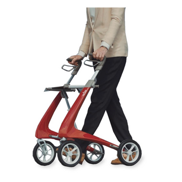 A person in a light sweater and dark pants uses the ByACRE Ultralight Carbon Fiber Rollator (10.6 lbs) with ergonomic handles and four large wheels, showcasing its sleek modern frame, on a white background.