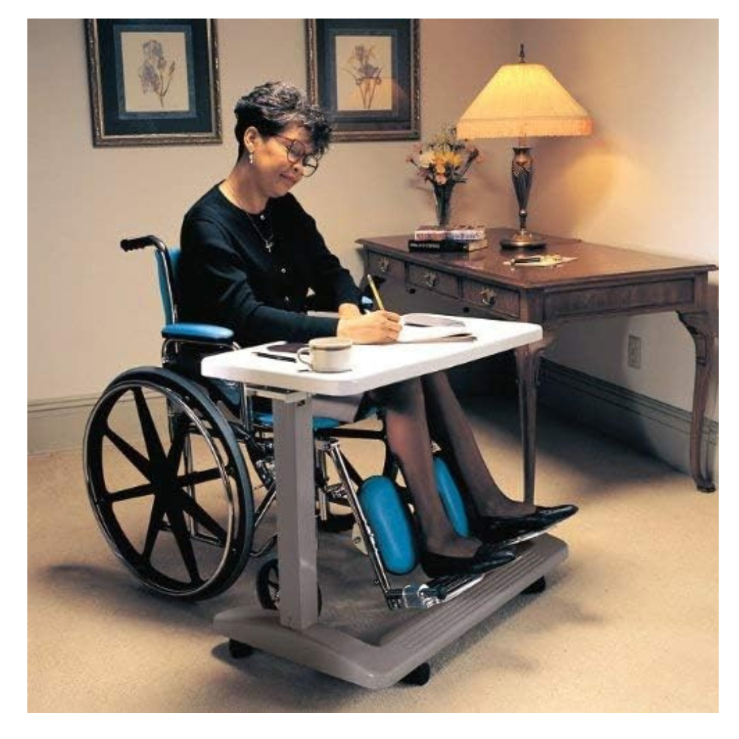 A woman in a wheelchair writes in a notebook at the Carex Height Adjustable Rolling Overbed Table with XL Surface. A cup and saucer sit on the table, surrounded by a lamp, flowers, and framed pictures in the cozy room.