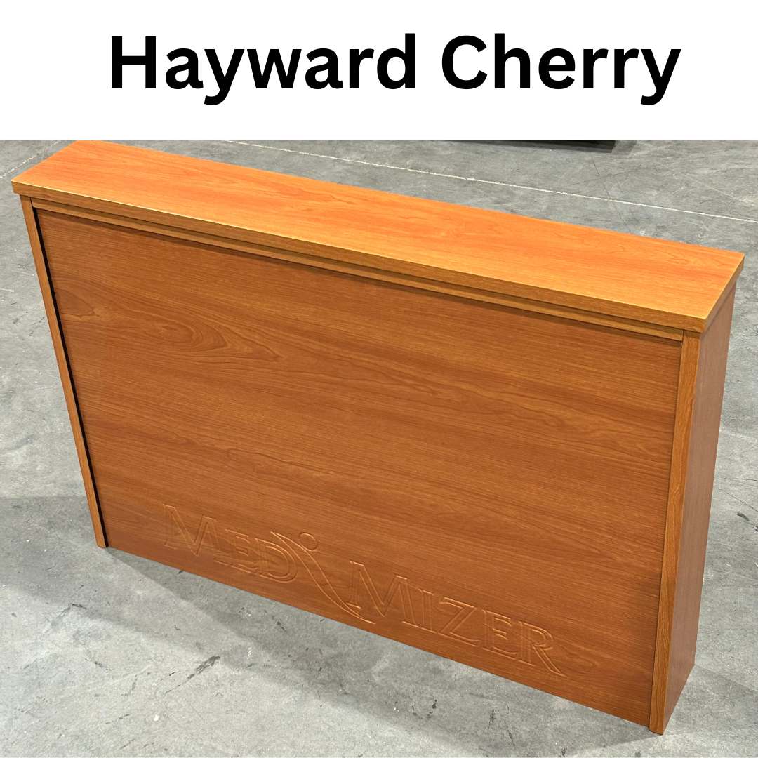 A wooden desk in a cherry finish labeled Hayward Cherry with MediVizer engraving sits on a gray concrete floor—ideal for pairing with the Med-Mizer ActiveCare Rotating Hospital Bed in any care setting.