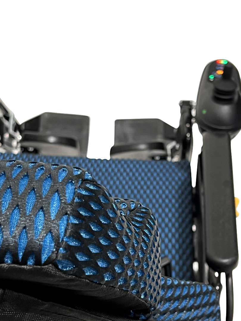 A close-up of the blue and black mesh seat on the ComfyGo X-9 Remote Controlled Powerchair highlights its sleek design. The right armrests control panel with colored buttons stands out, similar to a remote-controlled wheelchair, against a neutral background.