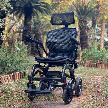 The EASWE B10 Portable Folding Powerchair - Airline Approved, featuring dual motors, mesh seat, headrest, and arm controls, is pictured on a dirt path in a lush garden with greenery and palm trees.