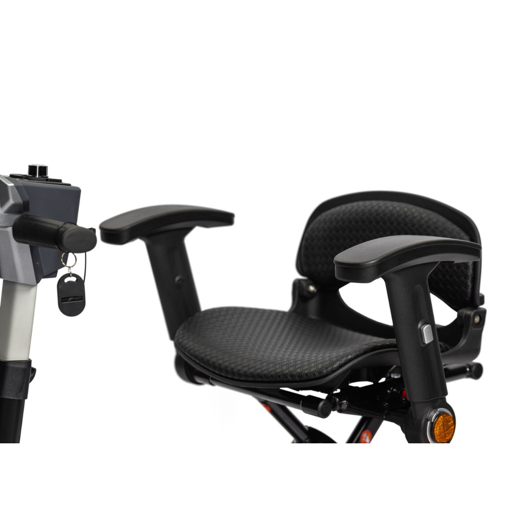 Close-up of the EV Rider Transport 4M Travel Scooter's black seat with armrests and textured cushioning. The lightweight scooter's handlebar and ignition key are visible on the left side of the image.
