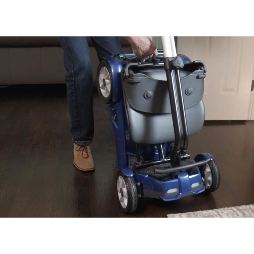 Someone folds the EV Rider Transport AF4W Automatic Folding Mobility Scooter upright on a dark wooden floor, getting the blue, compact scooter ready for storage or transport.