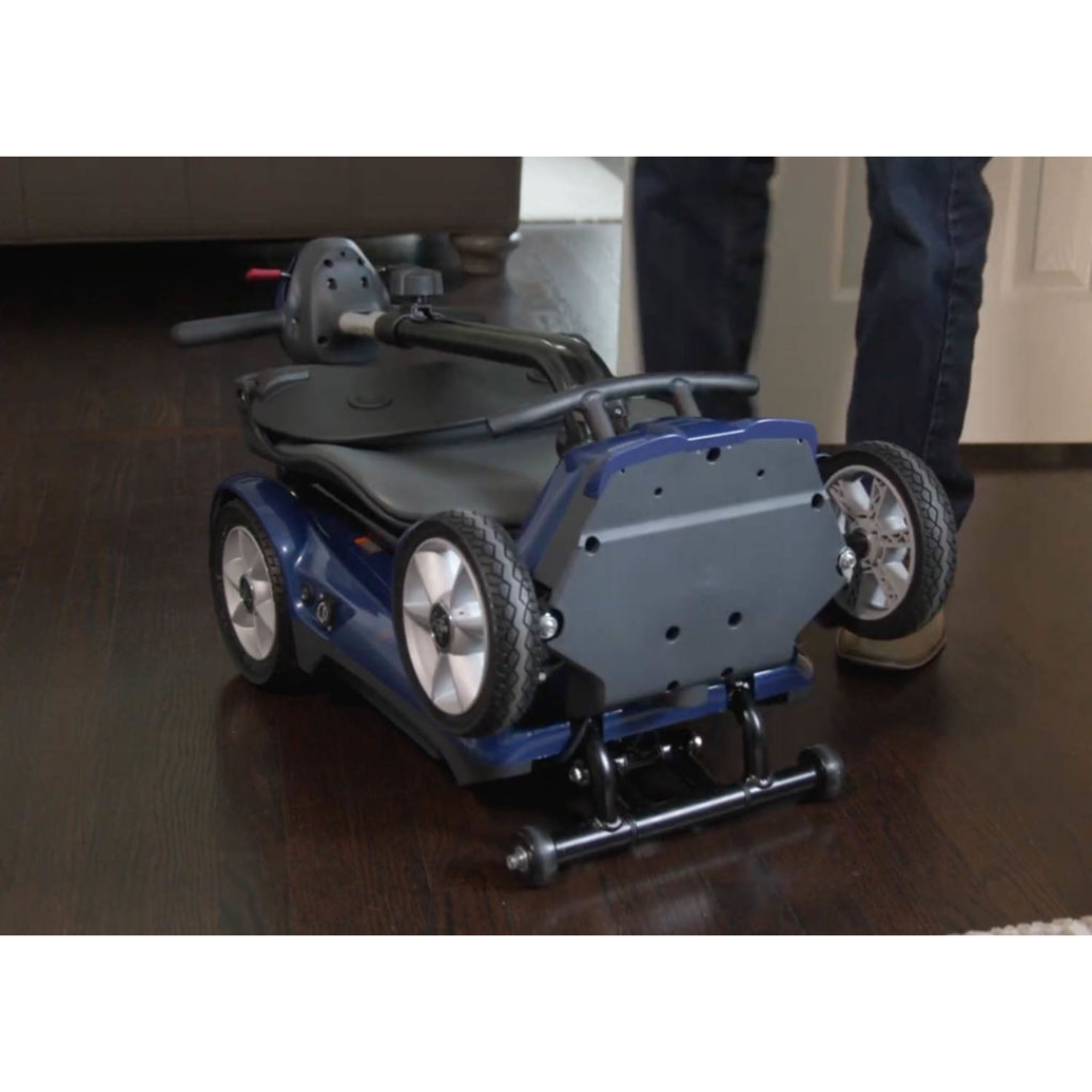 A person stands next to the EV Rider Transport AF4W Automatic Folding Mobility Scooter with a high-capacity lithium battery on a dark wood floor, ready for transport or indoor storage.