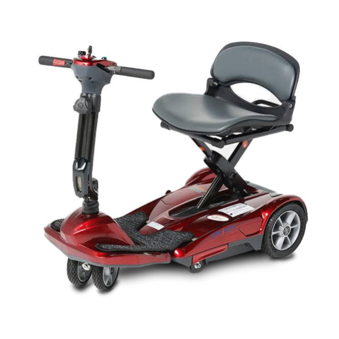 The EV Rider TranSport M Easy Move S19M Travel Scooter is a compact, red three-wheel scooter with small wheels, upright handlebars, and a padded gray seat with backrest. Its lightweight design and low platform make it ideal for easy personal transport.