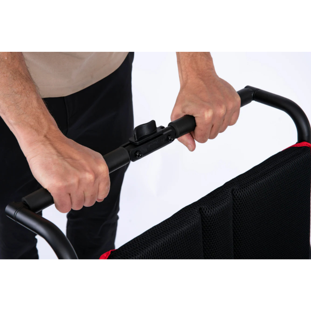 Close-up of hands gripping the handlebar of the Feather Powerchair, an ultralight electric wheelchair (only 33 lbs) with a black and red fabric backrest, shown against a white background.