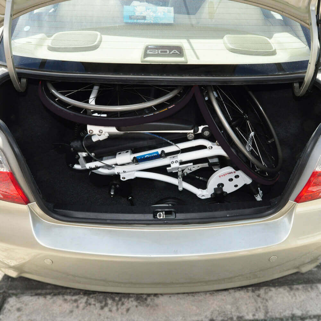 A folded white bicycle fits inside a beige car’s trunk, just as the Foldawheel Lloyd Pegasus Semi-Powered Standing Wheelchair can be compactly stored for easy transport.
