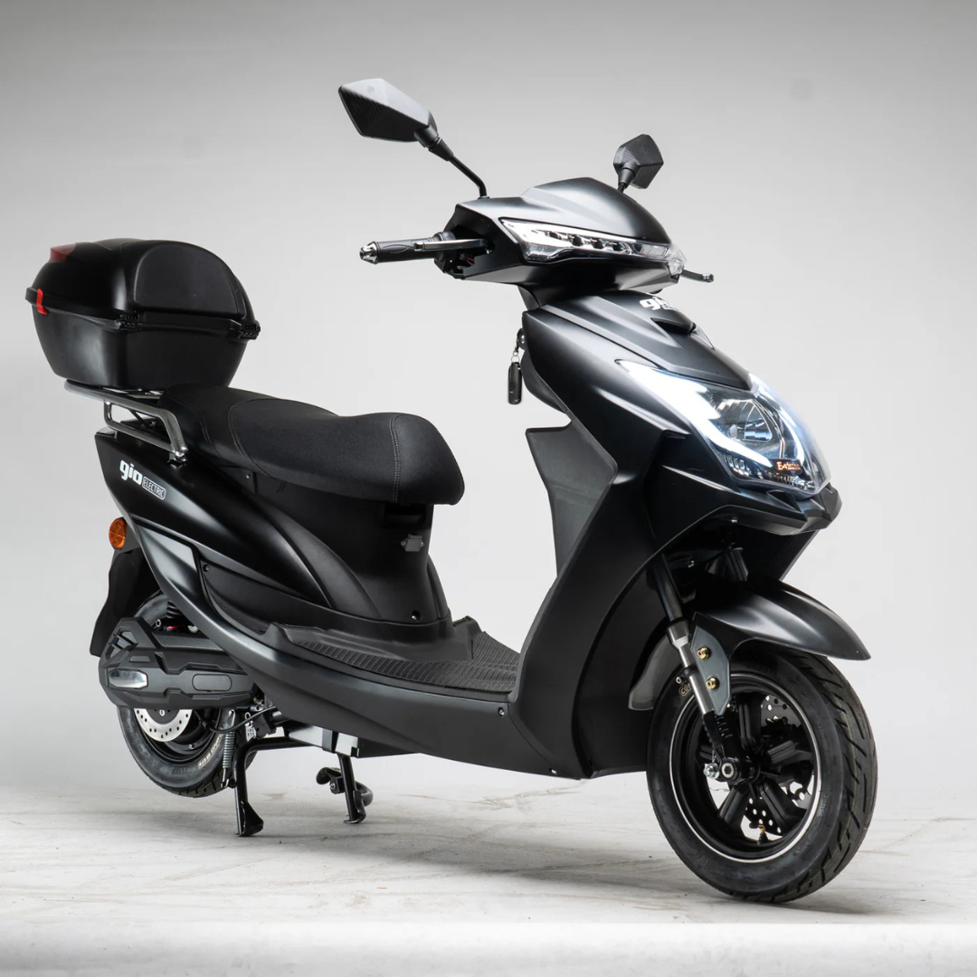 The GIO Phoenix Premium Electric Scooter, a stylish black eco-friendly ride with rear storage box, kickstand down, and modern LED headlights, is showcased against a plain light gray background.