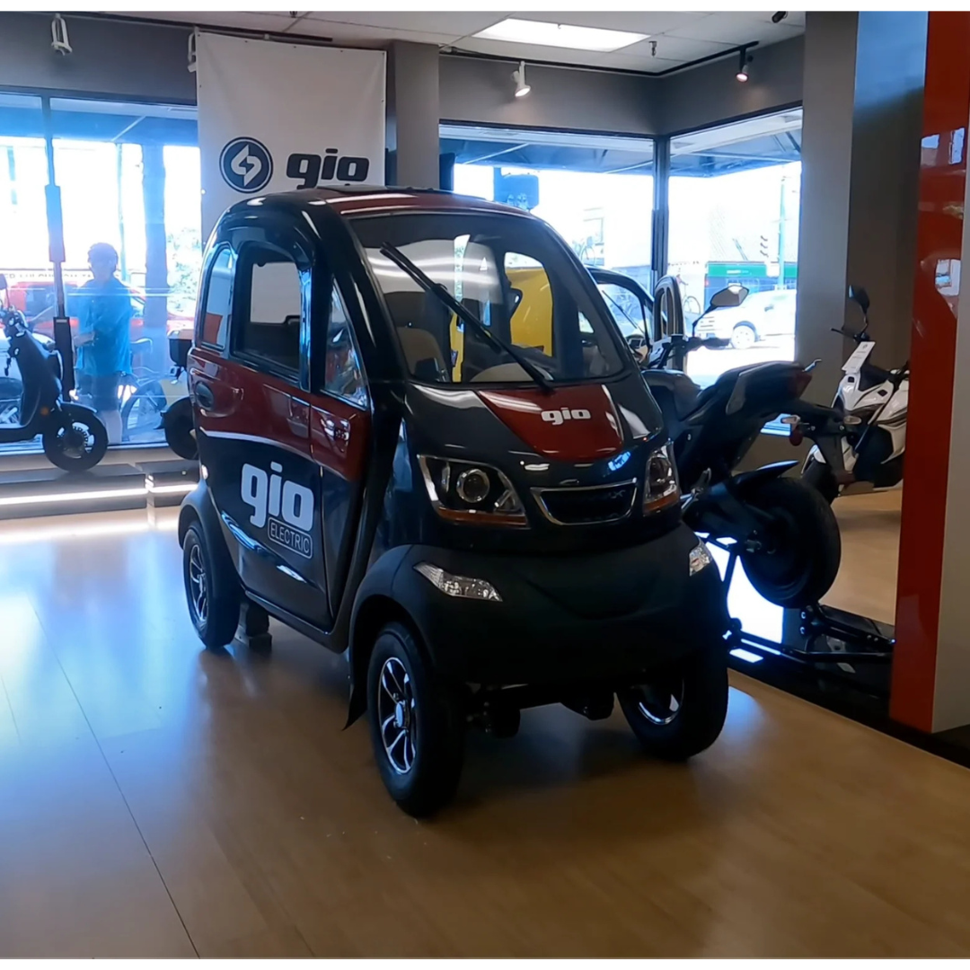 A GIO Golf Fully Enclosed Mobility Scooter with Heater and Cooling Fan, in red and black, is showcased inside a showroom with large windows; other motorcycles and scooters are visible in the background.