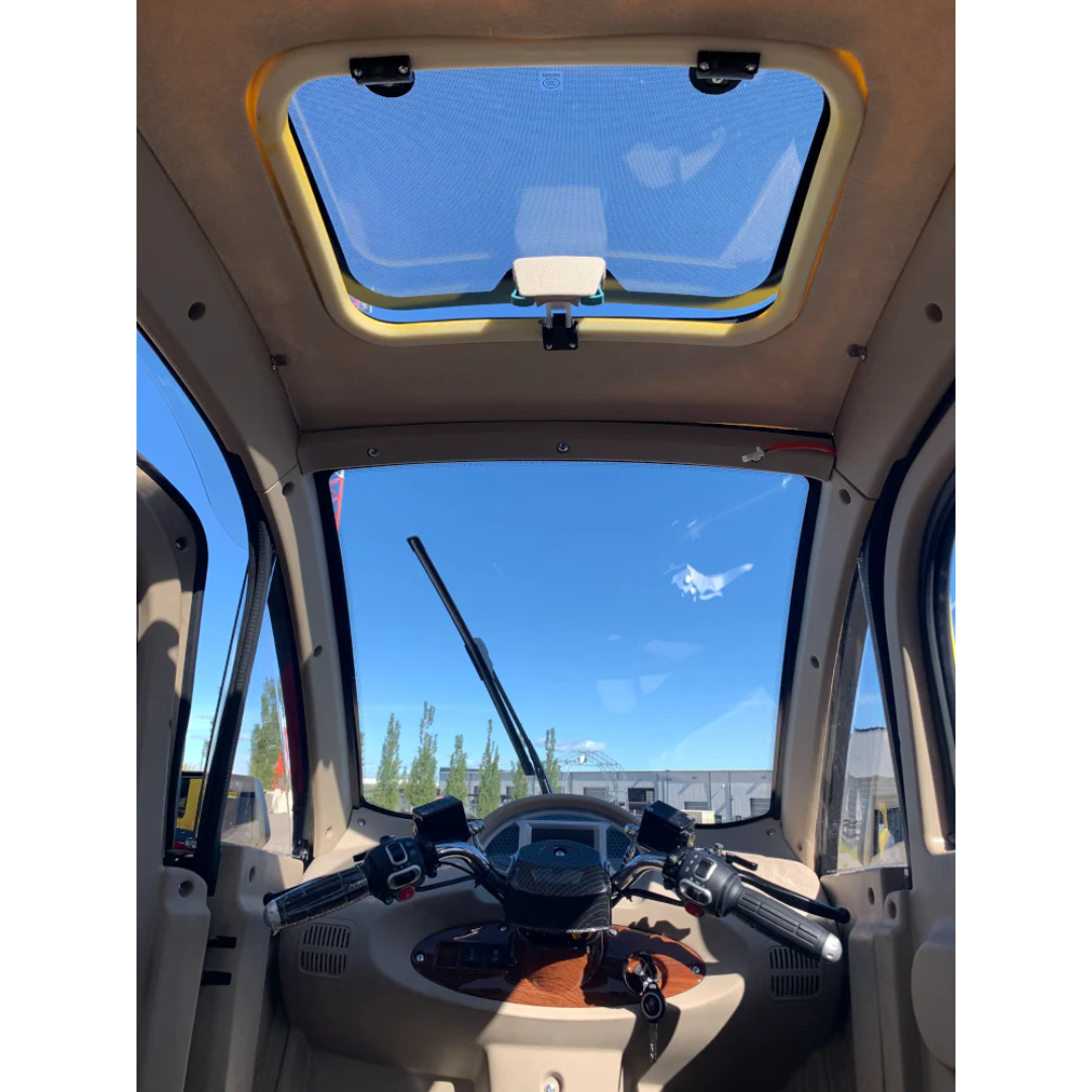 Interior of the GIO Golf Fully Enclosed Mobility Scooter with Heater and Cooling Fan, showcasing handlebars, dashboard controls, and a sunroof above, with blue sky and buildings visible through the windshield.