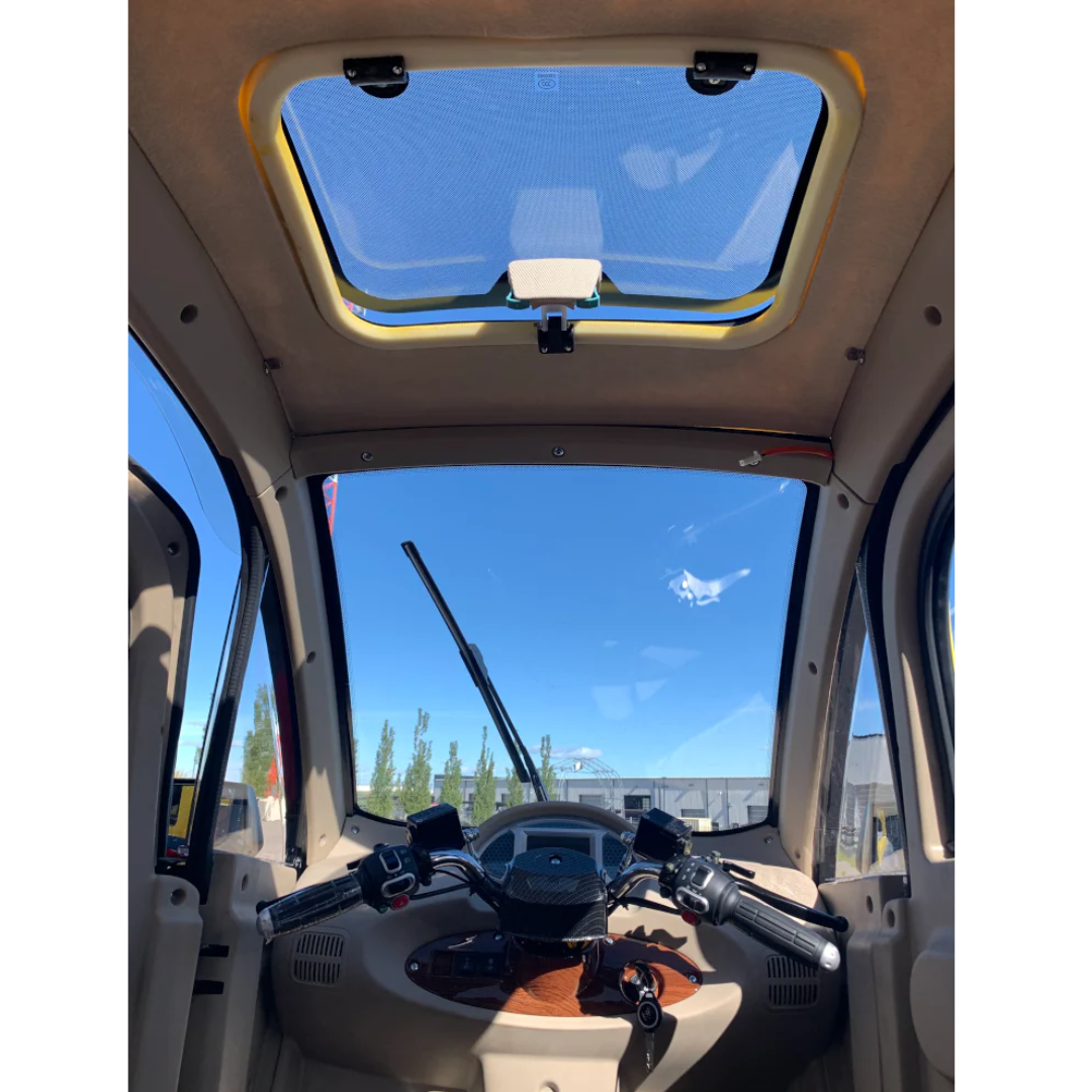 Interior view of the GIO Golf Fully Enclosed Mobility Scooter with Heater and Cooling Fan, showing a steering handle, windshield wiper, and large sunroof for scenic sky views with distant trees and buildings.