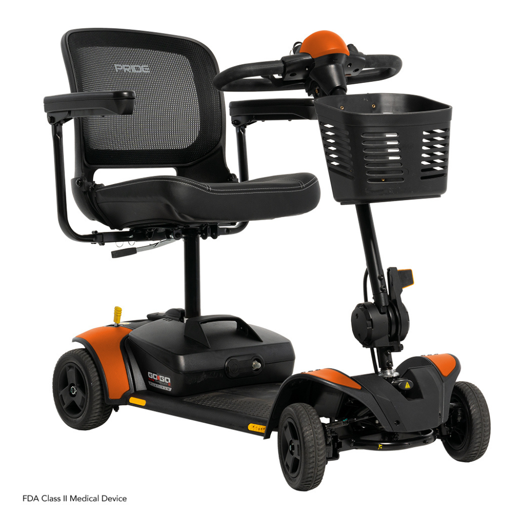 The Pride Mobility Go Go Elite Traveller® 2 Platinum Scooter is a black and orange personal transport with a mesh seat back, armrests, front basket, and four small wheels.