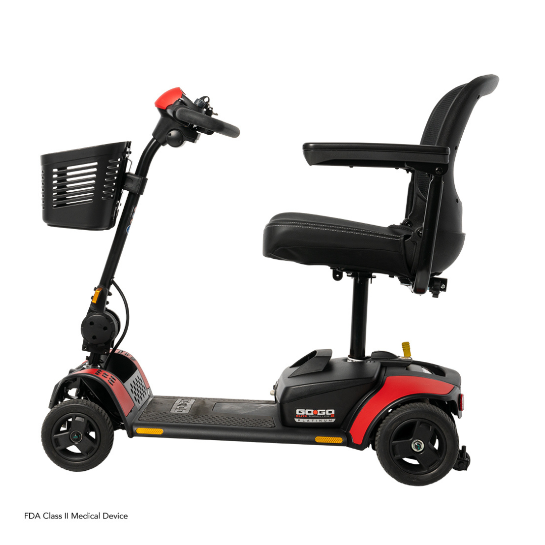 The Pride Mobility Go Go Elite Traveller® 2 Platinum Scooter is a three-wheeled travel scooter with red and black accents, black seat with armrests, and a front basket, shown side view against a white background.