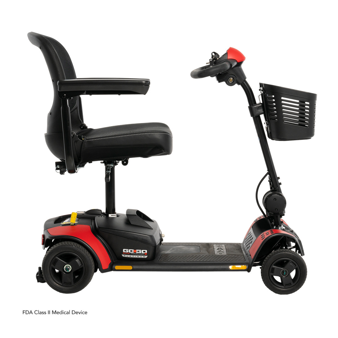 The Pride Mobility Go Go Elite Traveller® 2 Platinum Scooter is a three-wheel mobility scooter with a black seat, red and black frame, armrests, handlebar basket, and small wheels, shown from the side against a white background.