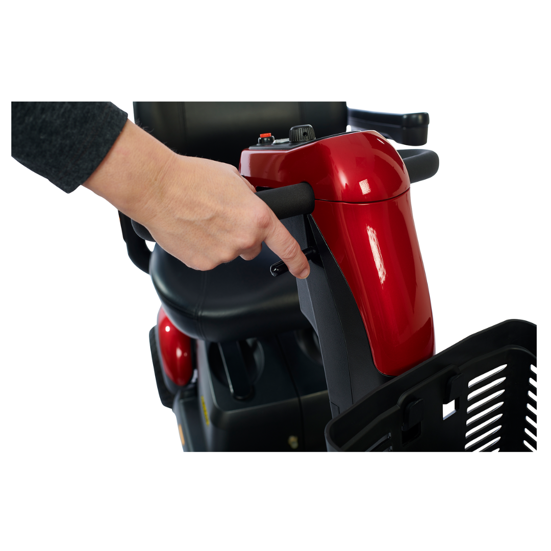 A person's hand is on the adjustable tiller of a Golden Buzzaround LX GB149 Heavy Duty 4 Wheel Portable Mobility Scooter, turning the speed knob. This red scooter features a black seat and a convenient basket at the front.