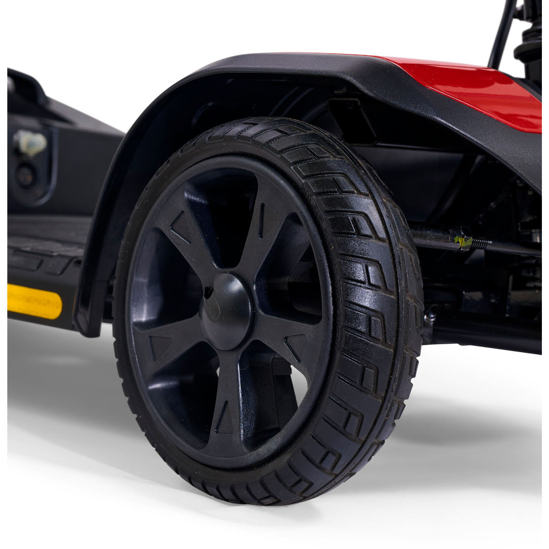 Close-up of a black, deep-tread wheel on a Golden Tech GB108 Buzzaround LT 4-Wheel Mobility Scooter with red and black trim and a lightweight stadium-style seat, shown against a white background.