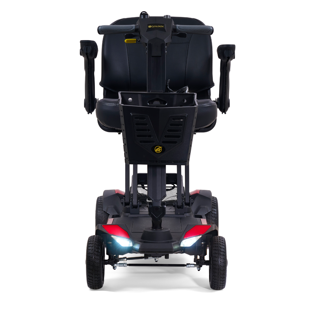 A front view of the Golden Buzzaround GB220 CarryOn HD Travel Scooter in black and red, featuring four wheels, headlights on, a basket, padded seat with armrests, and a 400 lb weight capacity.