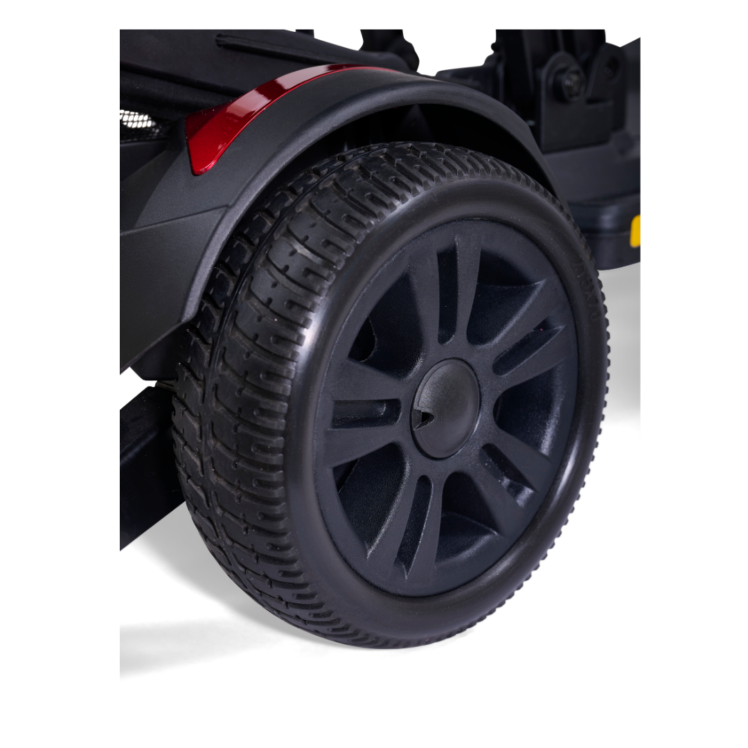 Close-up of a black rubber tire with textured tread and a black plastic rim on the Golden Buzzaround GB220 CarryOn HD Travel Scooter, with part of a red reflector visible above the heavy-duty wheel.