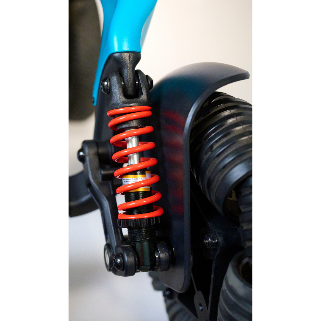 A close-up of the Golden Tech Ally Pro Smart All-Terrain Power Wheelchair showcases its bright red coil spring, highlighted against a neutral backdrop. The teal handlebar contrasts with the background, drawing attention to the vibrant color and robotic-like mechanical details.
