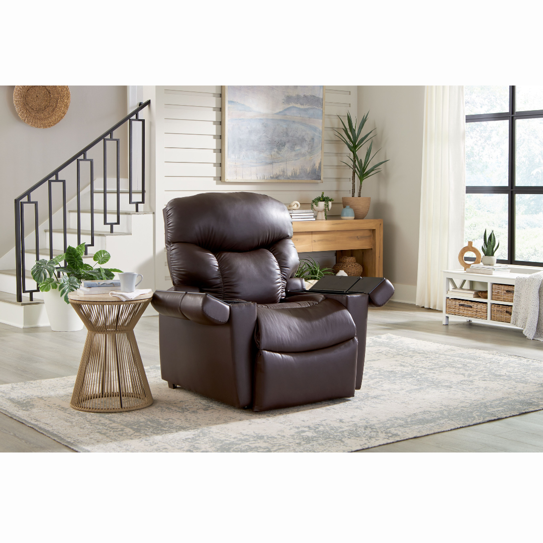A cozy living room showcases a Golden Cloud+ PR511 Recliner with Lift Assist - Medium Wide on a light rug. Nearby, a wooden side table hosts a cup and saucer. Plants and decor items adorn the shelf, while the AutoDrive hand control grants easy access to 4-Zone Comfort Zone settings for the chair.