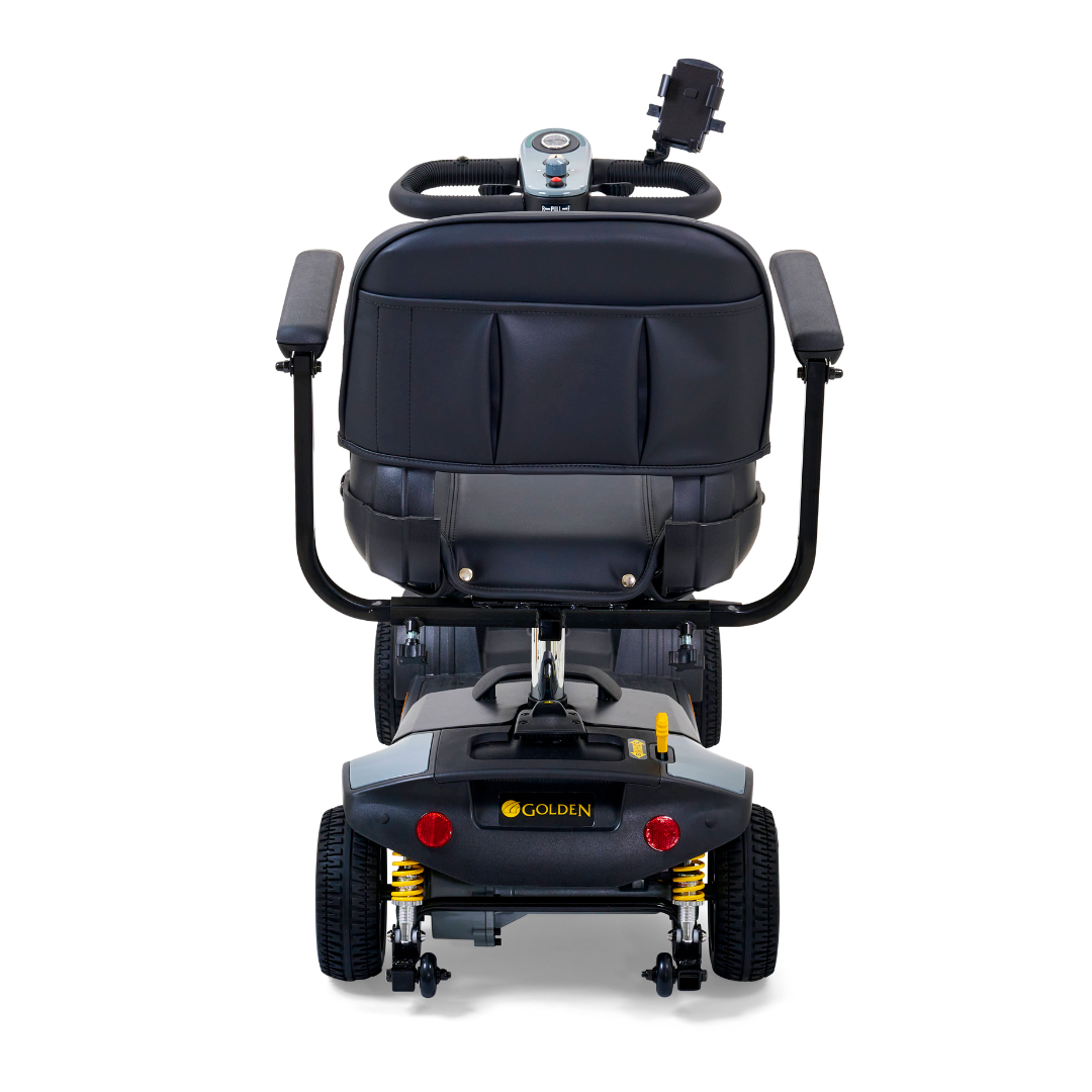 Rear view of the Golden Tech GB124 Buzzaround XLS HD features a cushioned seat, backrest, and Delta tiller handlebars. It has four wheels with Comfort Spring Suspension, a speed dial on its small dashboard, and the logo prominently visible on the rear.