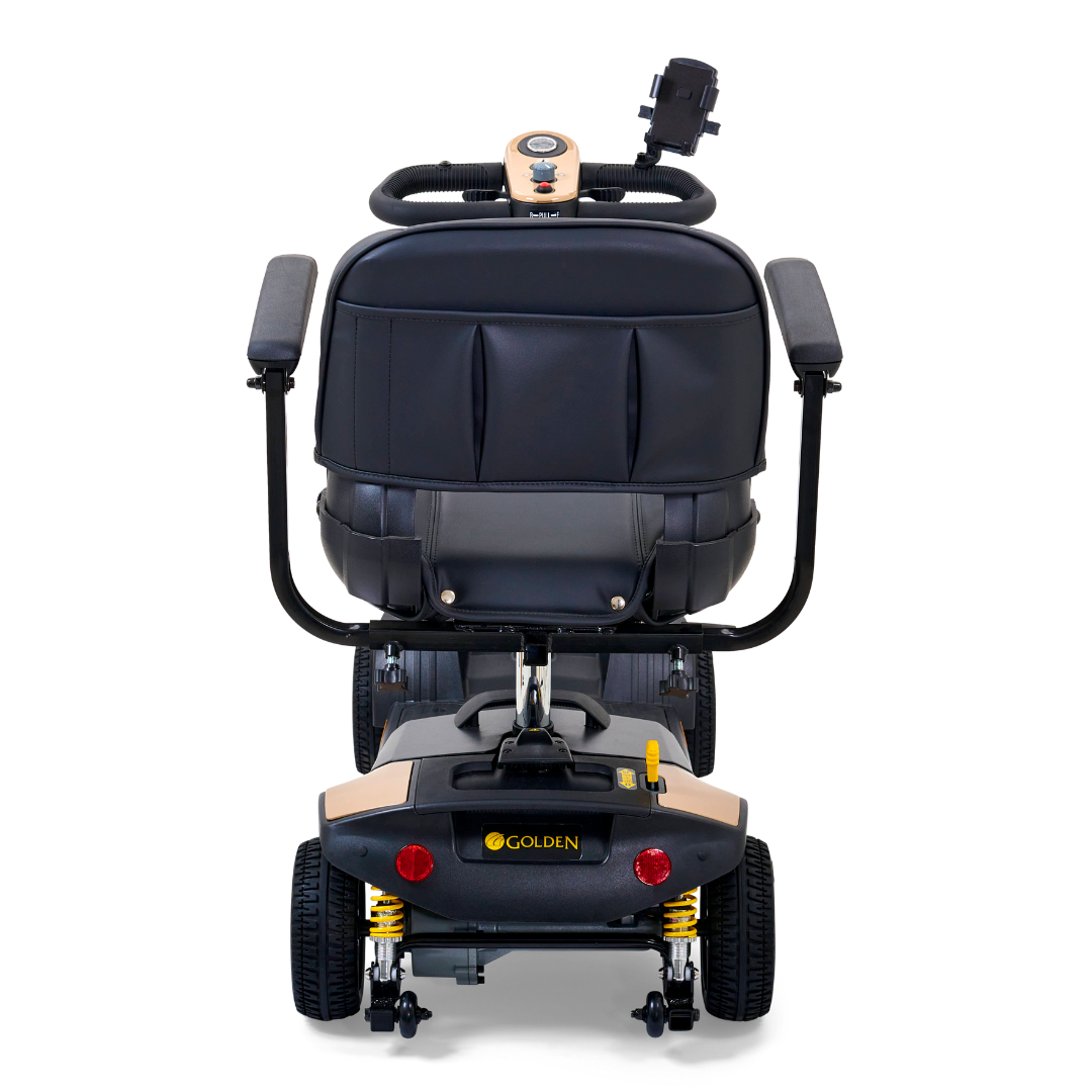 The Golden Tech GB124 Buzzaround XLS HD is a black 4-wheel portable scooter featuring armrests, a cushioned seat with Comfort Spring Suspension, a Delta tiller, and an under-seat storage compartment. The Golden logo is prominently displayed on the back for brand recognition.