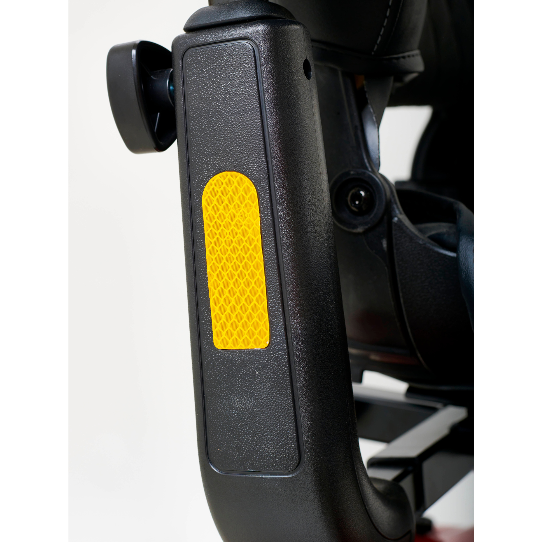 Close-up of a black wheelchair armrest featuring a yellow reflective strip, reflecting the safety-focused design of the Golden Tech GC340 Companion Full-Size Bariatric Mobility Scooter. The white background highlights the textured surface and reflective detail.