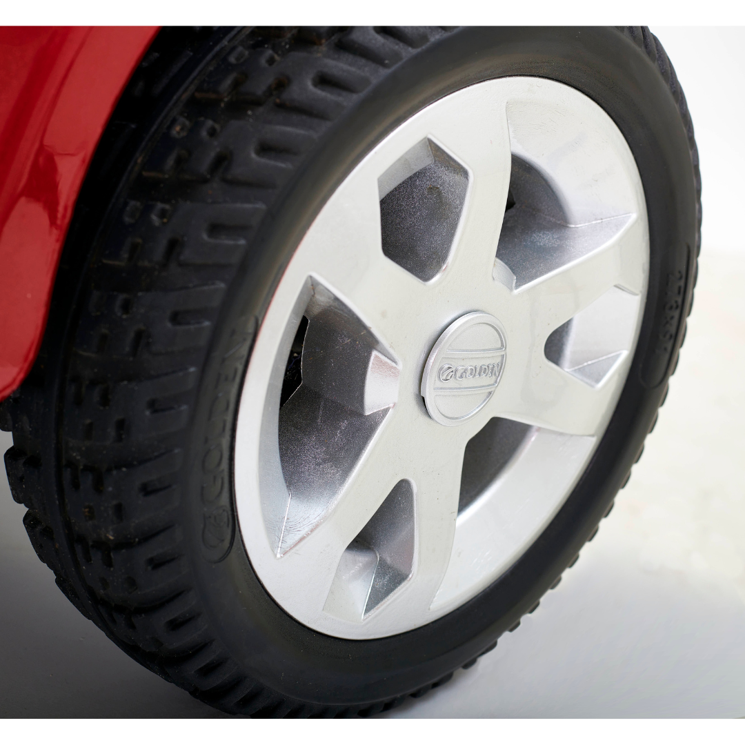 A close-up of a car tire with a silver alloy wheel featuring a visible tread pattern, attached to a red vehicle. The Casey brand shines from the wheel cap, its sleek design echoing the comfort of the Golden Tech GC340 Companion Full-Size Bariatric Mobility Scooter in light gray.