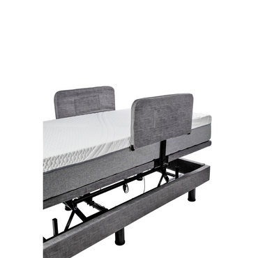 The Golden Tech Passport Homecare Bed features a gray fabric upholstered headboard, adjustable base with a white mattress, and raised frame to expose mechanical components, blending modern style with essential accessories for enhanced safety.