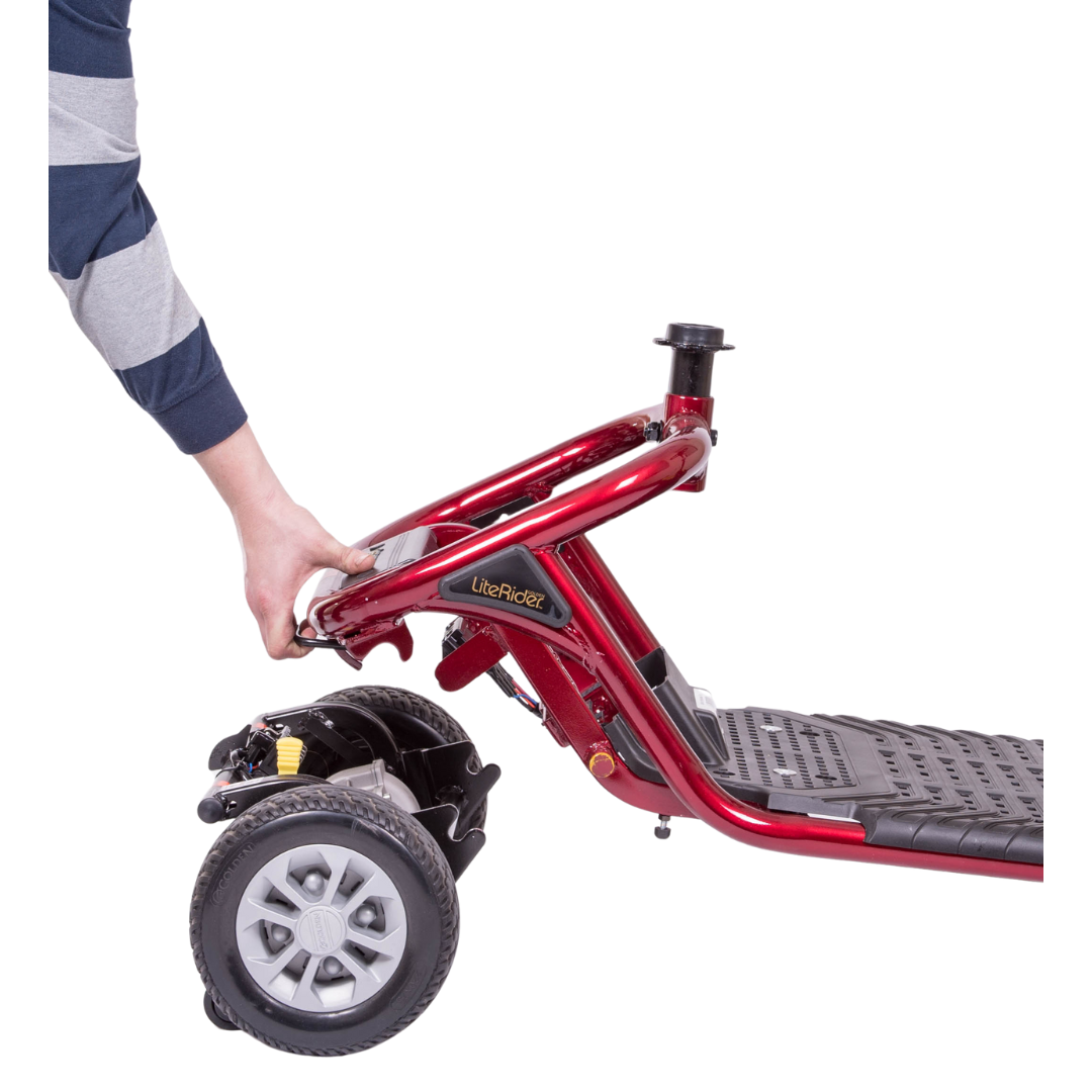 A person folds a red Golden Tech GL111 LiteRider 3-Wheel Mobility Scooter with a Delta Tiller by lifting the platform. It features a gray footrest and rear wheels. The individual wears a long-sleeve shirt with blue and gray stripes.