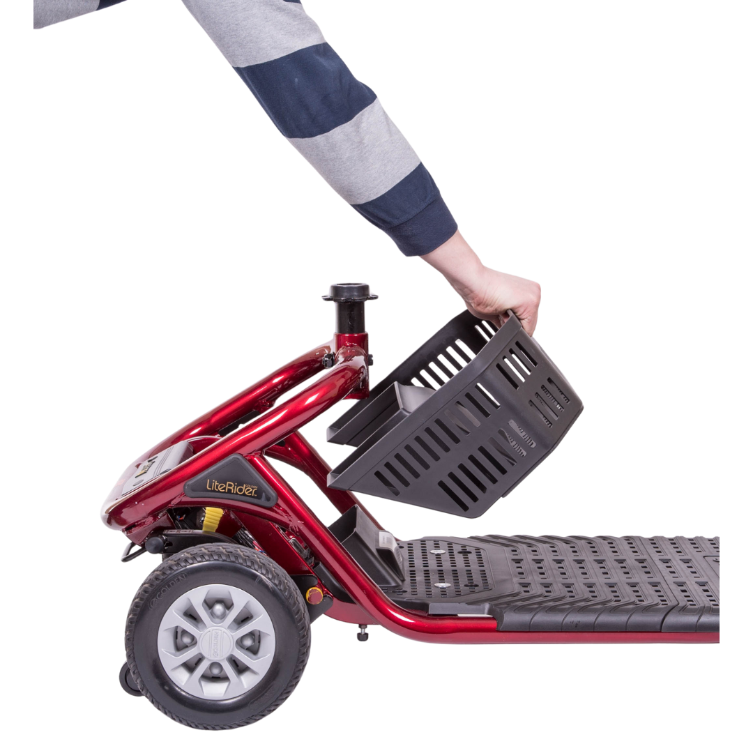 A person in a striped sleeve attaches a black basket to the front of a red Golden Tech GL111 LiteRider 3-Wheel Mobility Scooter, showcasing its logo on the frame. The scooter has a visible wheel and footrest, designed for easy wireless disassembly.