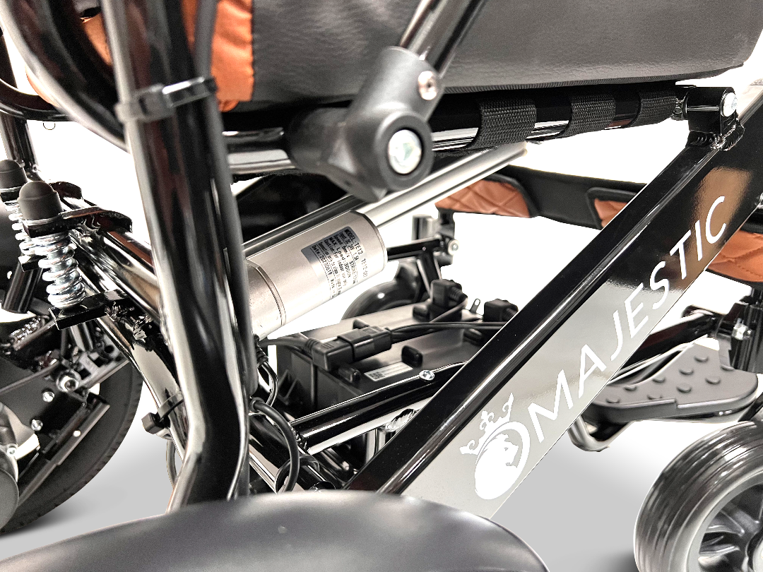 Close-up of the ComfyGo MAJESTIC IQ-9000 Auto Reclining Electric Wheelchair, showing its aircraft-grade aluminum alloy frame, suspension, battery compartment, digital joystick controller, and seat with orange accents.