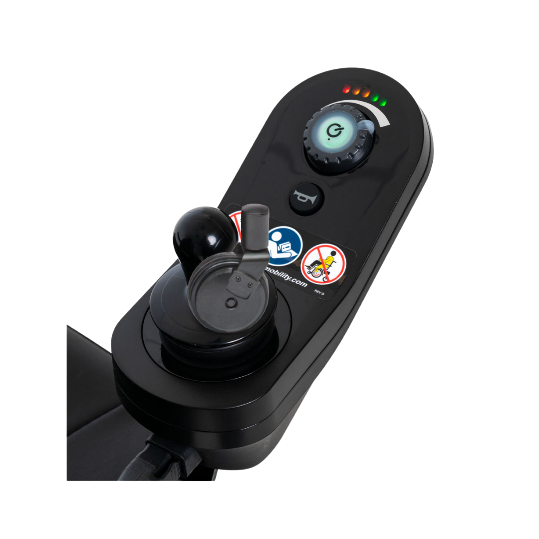 A close-up of the Pride Mobility Jazzy® 600 ES Powerchair’s black joystick control panel shows a power button, battery indicator lights, and control stick, highlighting advanced maneuverability and warning stickers against standing on the device.