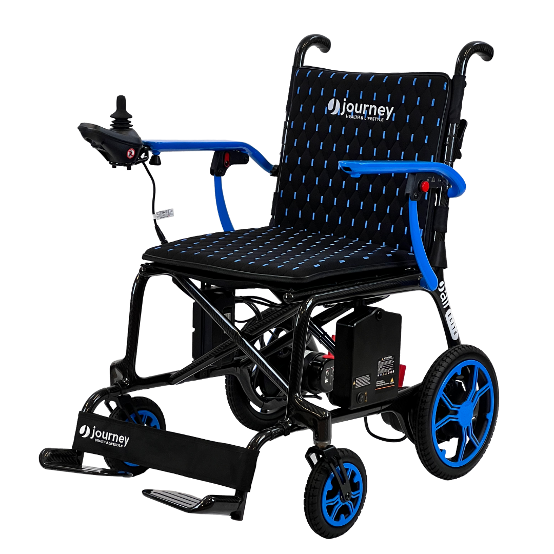 The Journey Air Elite Folding Carbon Fiber Powerchair weighs only 29 lbs, featuring a black seat with blue accents, rear wheels, armrest joystick controller, footrest, and sleek black frame. Its travel-friendly design includes an easily accessible battery pack underneath.