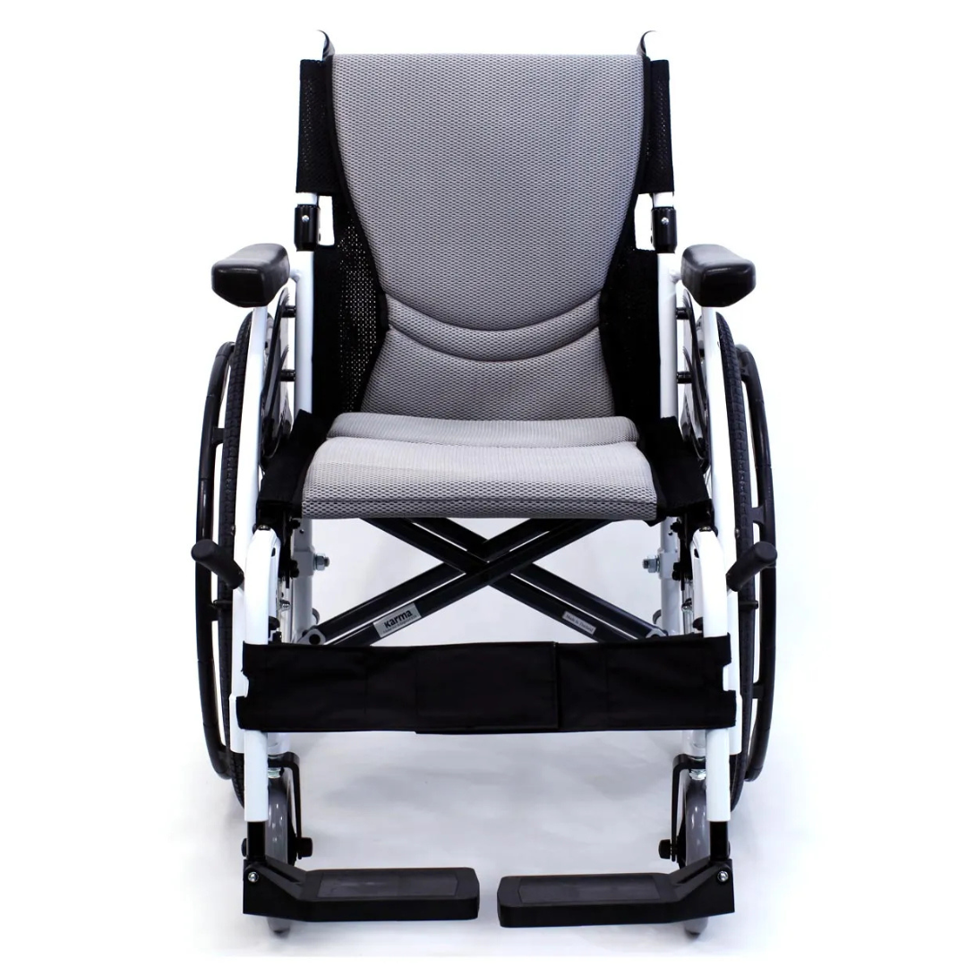 The Karman S-Ergo 115 Ultra Lightweight Ergonomic Wheelchair, weighing only 25 lbs, boasts ergonomic seating with a light gray cushioned seat and black armrests. Its sleek design features large rear and small front wheels with a primarily white frame accented in black for mobility and comfort.