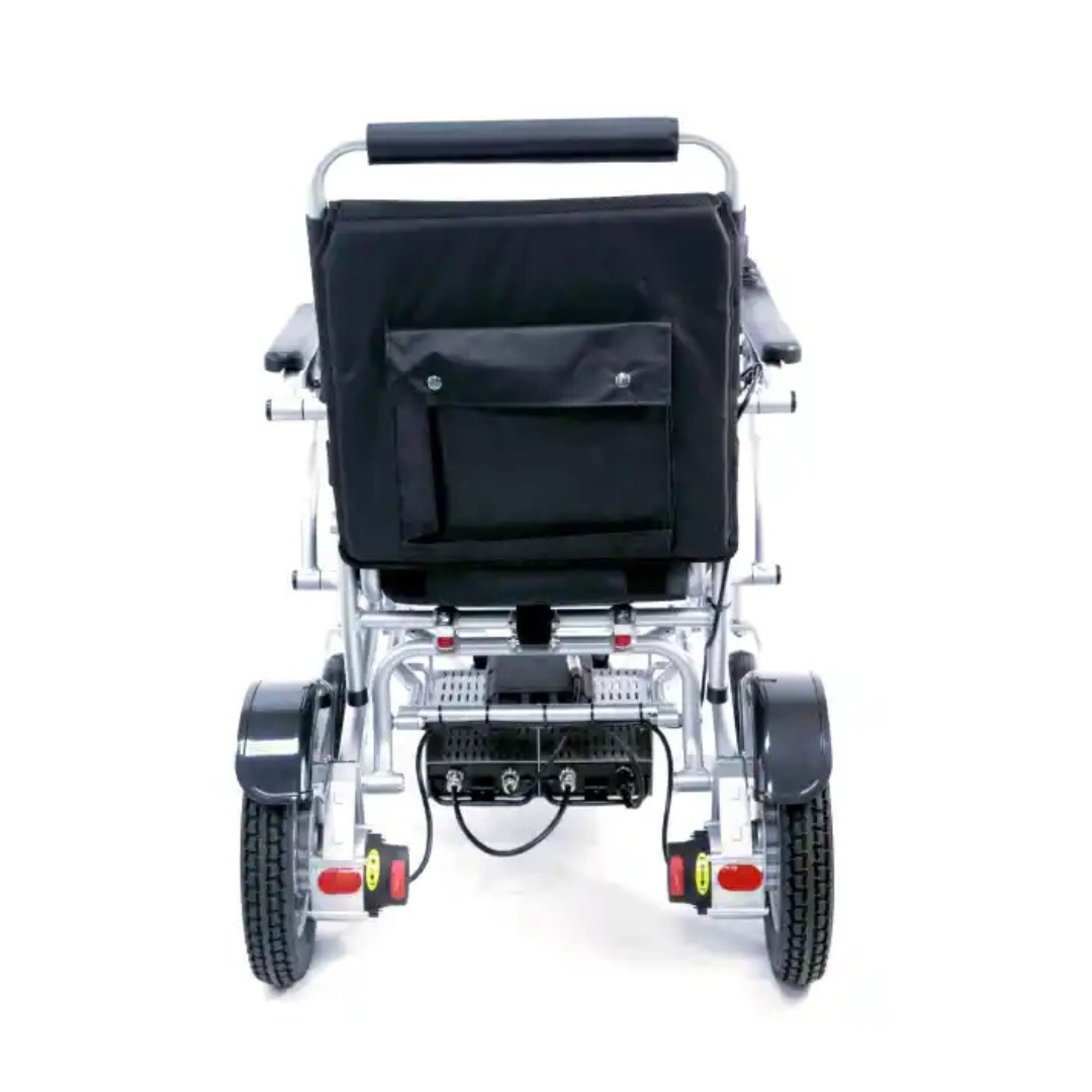 The Karman Tranzit Foldable Lightweight Power Wheelchair features a black seat and backrest. It includes large, sturdy wheels, a battery pack beneath the seat, and a small pocket on the backrest. Its foldable silver metal frame adds to its lightweight design. FAA approved for travel.