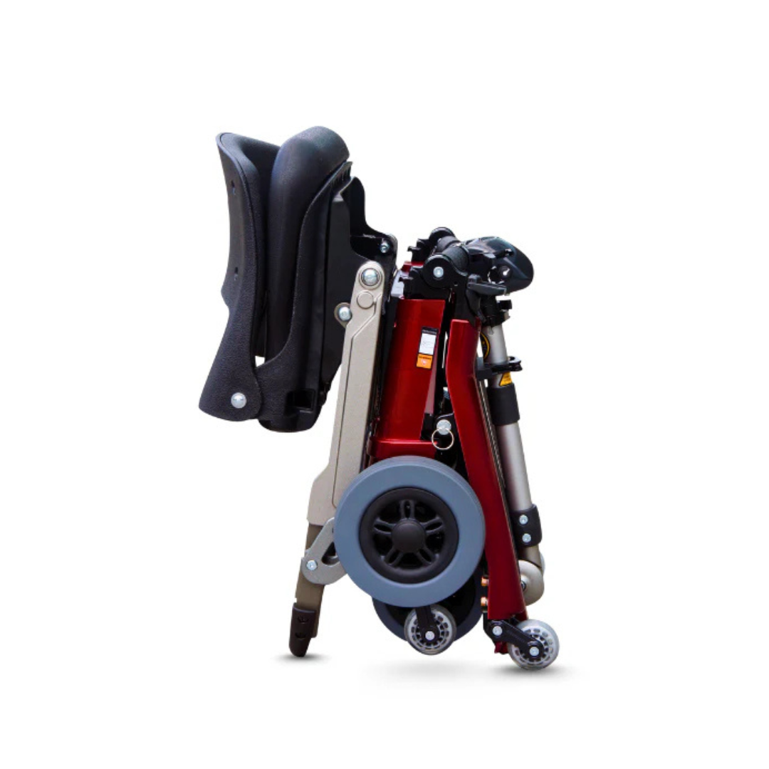 The FreeRider Luggie Elite Travel Scooter, airline approved with a black seat, red frame, large rear wheels, and small front caster wheels, stands compact and folded upright on a white background.