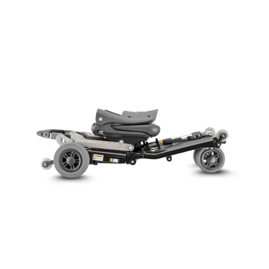 The FreeRider Luggie Elite Travel Scooter, a compact and foldable model with gray wheels and a black frame, is pictured collapsed and lying flat on a white background.