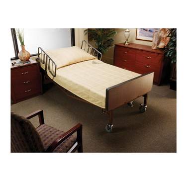 A homecare bed with side rails and a Medline Premium Foam Homecare Mattress (36” x 80” x 6”) sits in a carpeted room with wooden dressers, a cushioned chair, a plant, and a framed wall picture. The bed features a beige quilted cover.